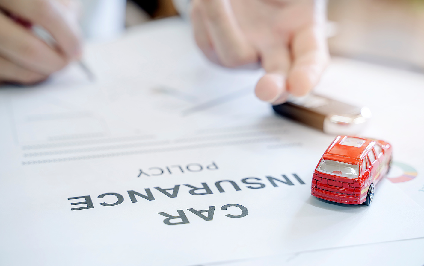 Car insurance policy with red car toy and blurred image of man hand for vehicle insurance policy concept.
