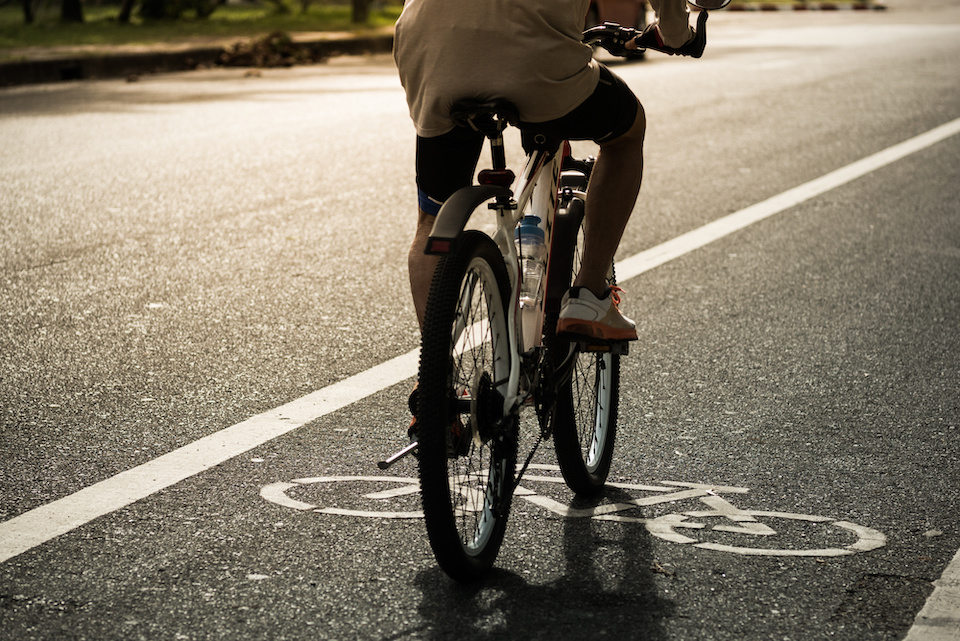 An old man riding a bicycle in the bike lane in the evening sunlight. Depicts bicycle lane rules.